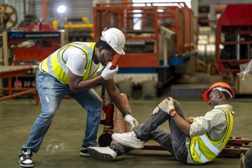 African American factory worker having accident while working in manufacturing site while his colleague is asking for first aid emergency team using walkie talkie radio for safety. workplace injury concept.