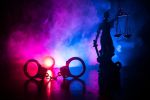 Legal law concept. Silhouette of handcuffs with The Statue of Justice on backside with the flashing red and blue police lights at foggy background. Selective focus